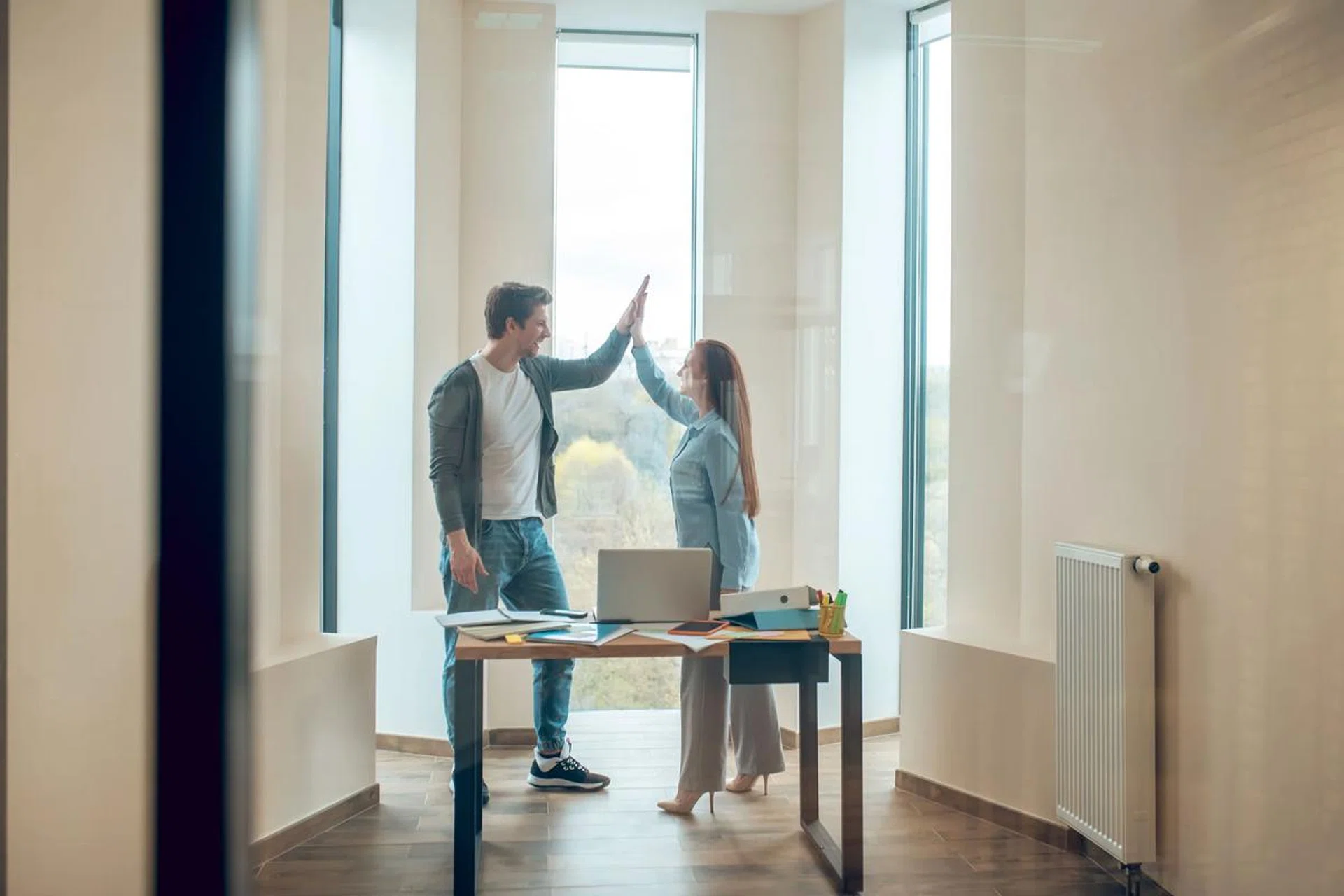Young business people working together in office. Businessman and businesswoman using laptop and talking while standing near window. Photo 123RF