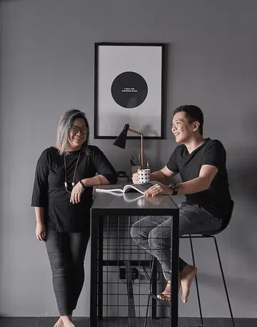 Interior designer couple, Sherlynn Low, and husband Brandon Chen posing at their dining table in their all black 5-room HDB BTO flat in Bukit Batok.