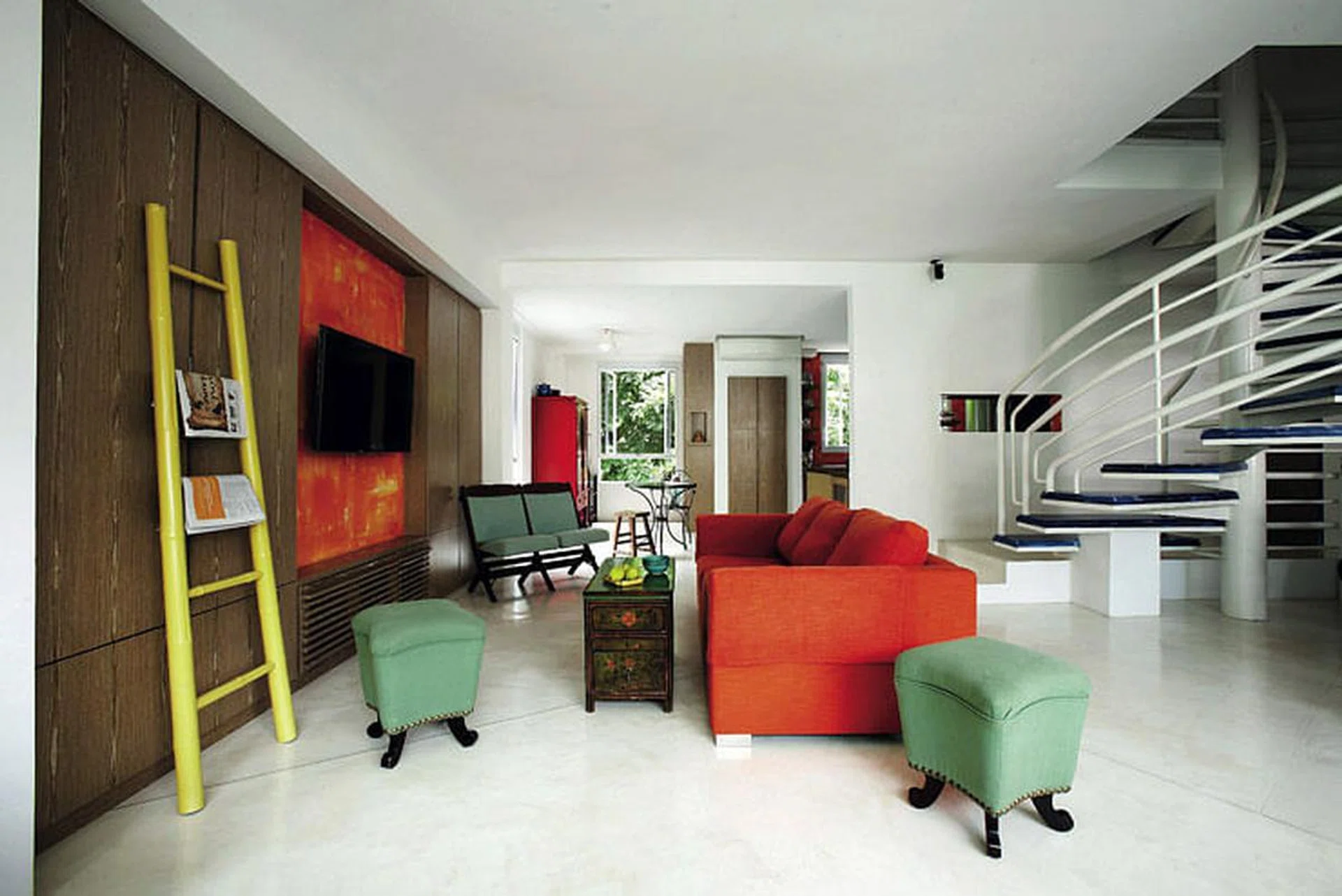 Shots of brilliant orange from the sofa and hand-painted feature wall anchor the colour scheme of the living room.