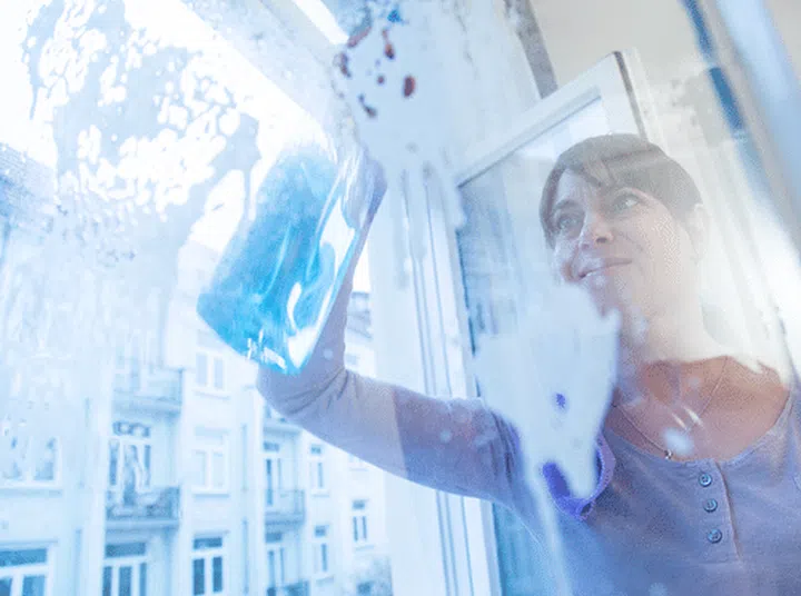 Brunette woman holding a spray bottle of detergent and cleaning a glass door or window. Photo: Christin Klose, Deutsche Presse-Agentur