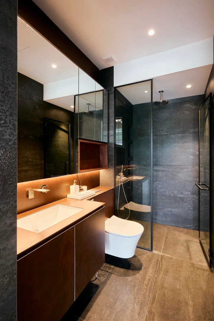 The master bathroom combines darker textured tiles with warm lighting, balancing depth with clarity.