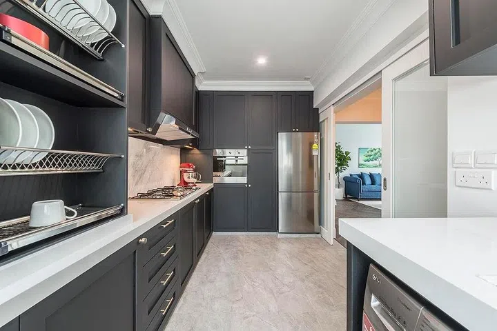 This grey kitchen features wainscoted cabinetry in EDL's Fenix laminate and a marble backsplash. The small counter space opposite the sink houses the washer and gives the couple extra food prep space. Interior Design by Aiden T.