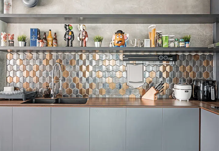 The grey laminate and wood-look Kompacplus countertop complement the gold and silver accented backsplash. The shelves offer the homeowners a space to showcase their interesting knick knacks. Interior design by DB Studio.