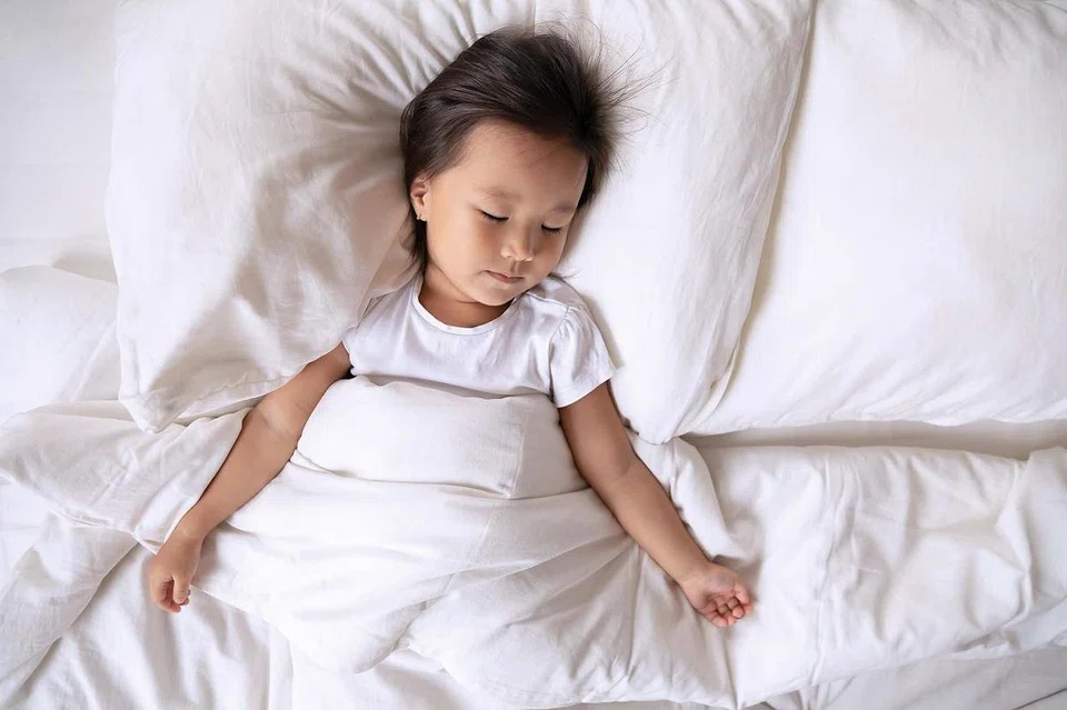 Asian little kid girl sleeping in bedroom on bed lying under warm duvet on comfortable mattress, top above view. Healthy peaceful sleep. Ad of high-quality diapers, great overnight protection concept