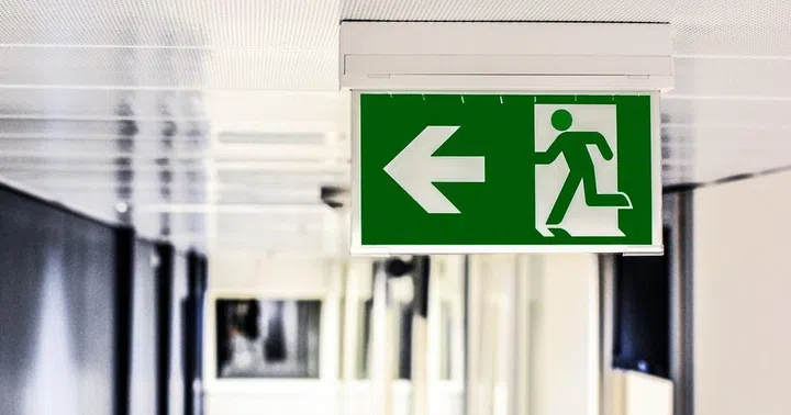 An emergency exit signage pictured against a white corridor. What fire safety regulations are there for high-rise buildings in Singapore?
