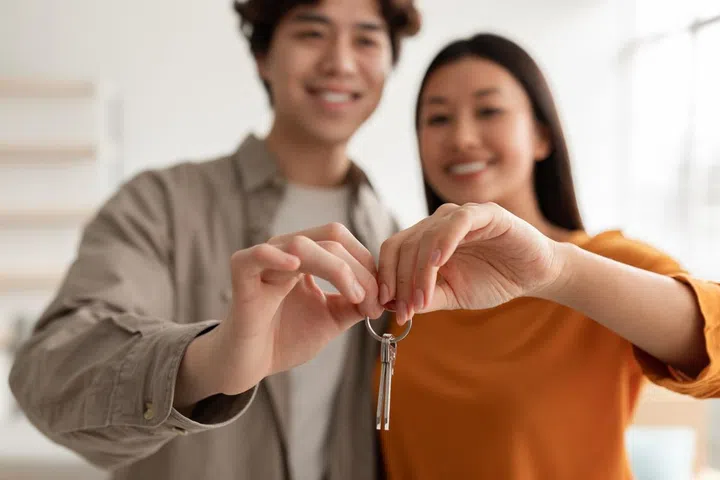 Happy millennial Asian couple showing house key, moving to new apartment together, selective focus