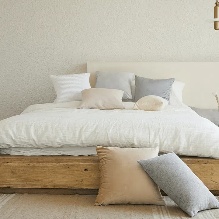 A stack of pillows and cushions strewn over a wooden bed with white bedsheets.