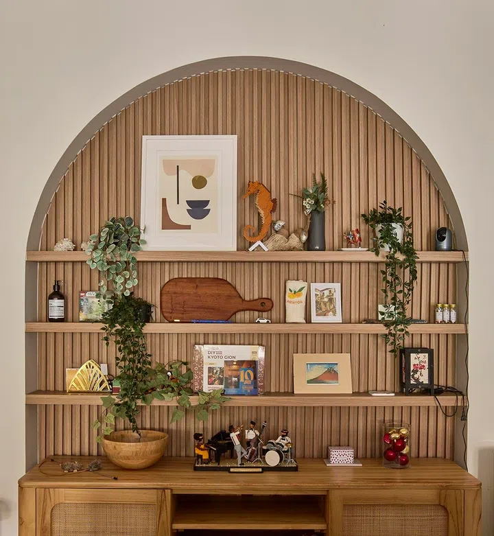 The arched niche, lined with fluted timber, doubles as display and storage, where personal objects and collected pieces bring warmth and character to the living room.