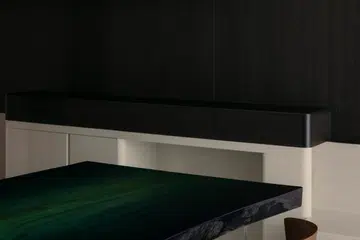 A custom dining table made from Japanese zelkova and dyed with natural indigo grounds the dining area against dark timber joinery.