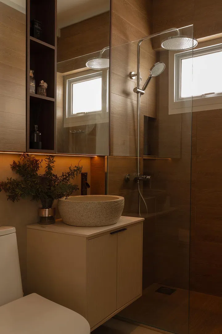 Wood-look tiles, built-in niches, and concealed storage behind the mirror maximise function within a compact master bathroom.