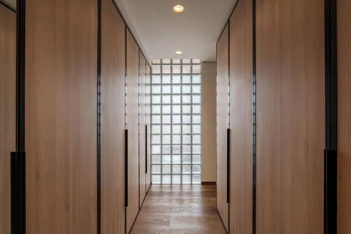 Full-height wardrobes line the walk-in dressing area, where borrowed light softens the functional storage zone.
