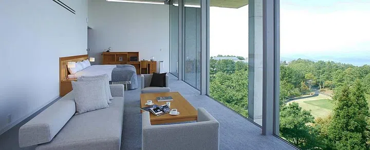 Setouch Aonagi designed by Tadao Ando. Hotel room view, showing the bed, sofa, and the clear glass window that overlooks a green garden