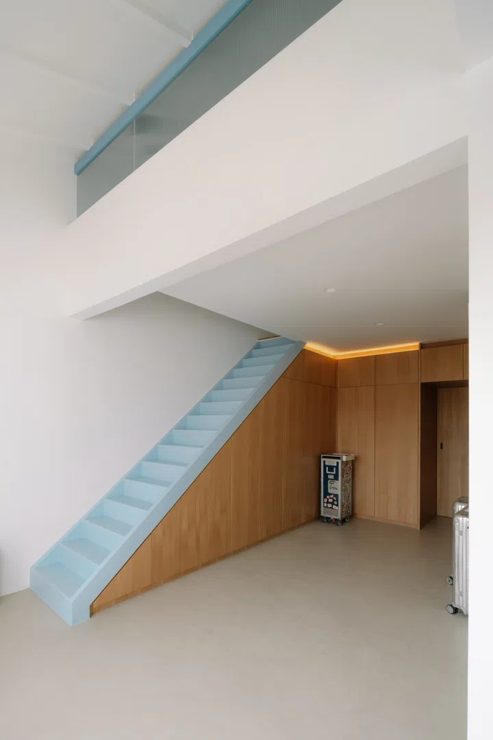 Tucked beneath the pale blue staircase, the walk-in wardrobe is lined with full-height bespoke oak cabinetry that maximises storage while maintaining the home’s restrained material palette.