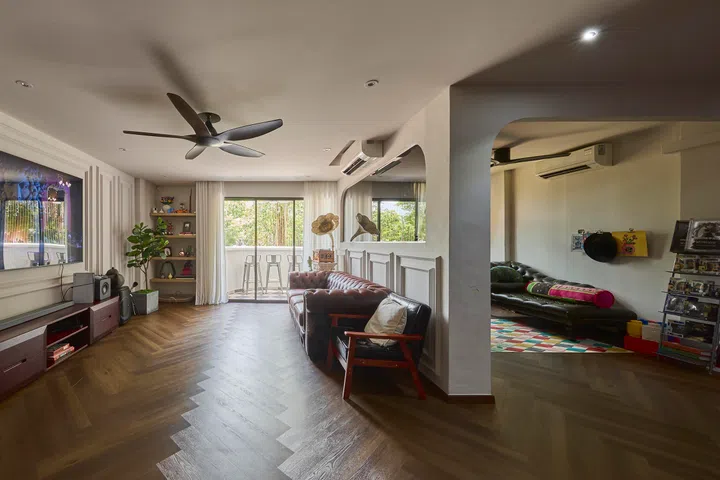 Natural light draws the eye through the living area towards the balcony, where classical wall mouldings meet an eclectic mix of furniture, art, and everyday objects.