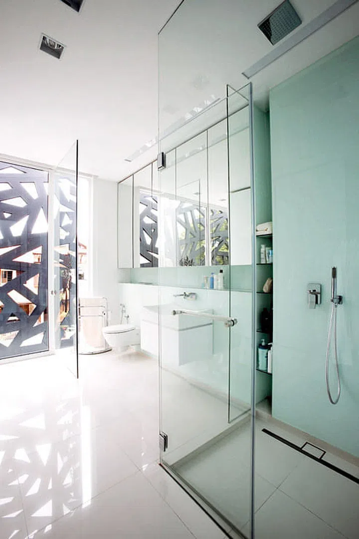 Despite its glass cubicles and floor-to-ceiling windows, the master bathroom is still safe from prying eyes, thanks to the cut-out metal screen. Glass, mirrors as well as all-white tiles and bathroom fixtures make this space look bigger and brighter than it really is. Interior design by Spacedge
