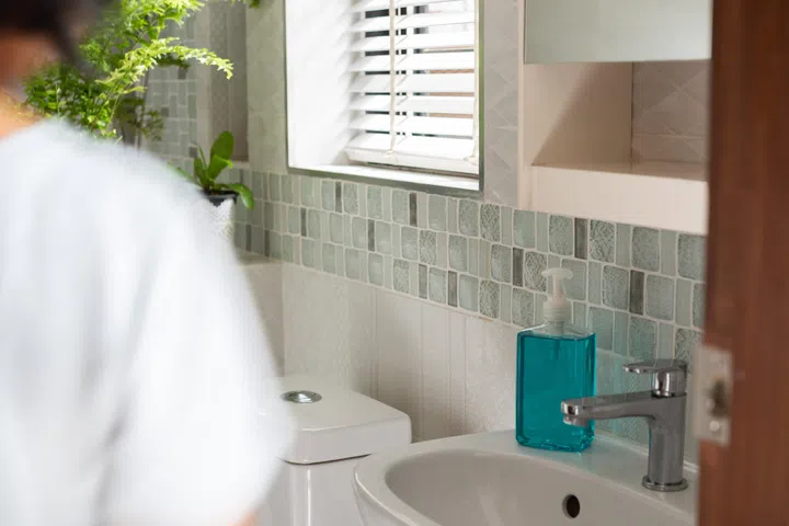 Blurred woman in modern bathroom or restroom with hand sanitizer to protect from coronavirus