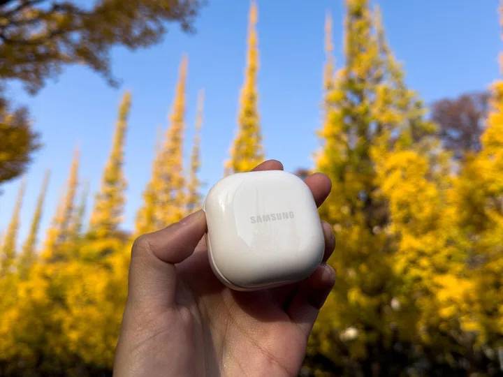 Hand holding white, standard Samsung earbuds case.