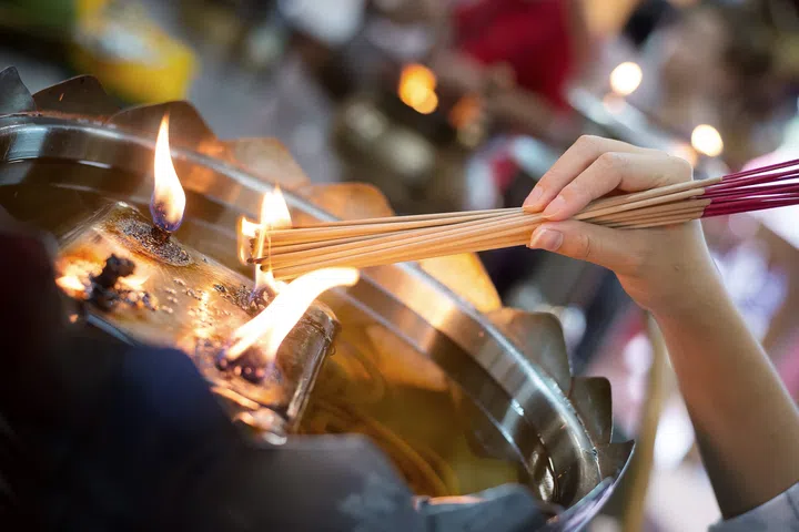 Girl grip and light the incense sticks from fire burning on oil lamp in temple.