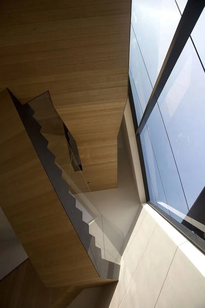 Ground-up view of the oak and glass stairwell. Glass windows open up to the pastel blue skies.