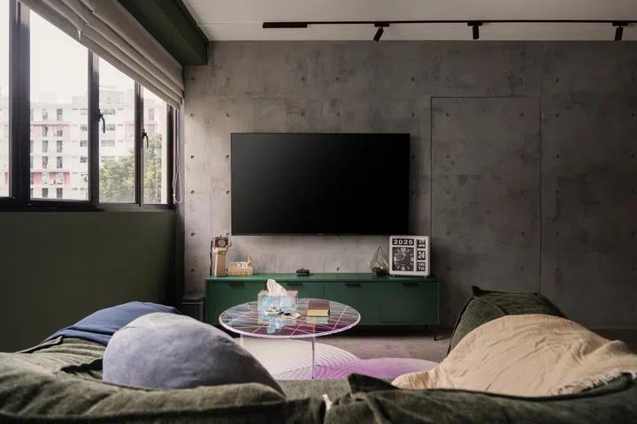 A full-height concrete wall anchors the living space, with a convertible sofa and textured TV backdrop adding comfort and character.
