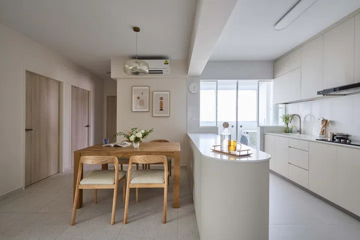A cream, curved kitchen island runs along the kitchen in a minimalist 5-room HDB BTO in Tampines.