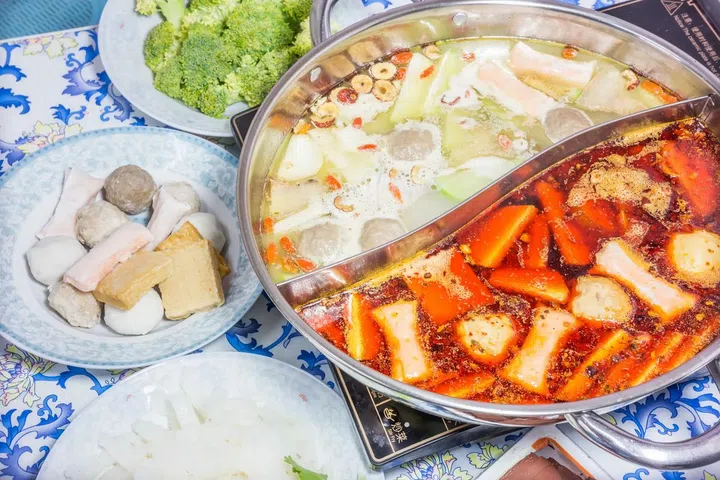 Half half Steamboat pot with two soup flavours and side dishes next to it. Photo 123RF