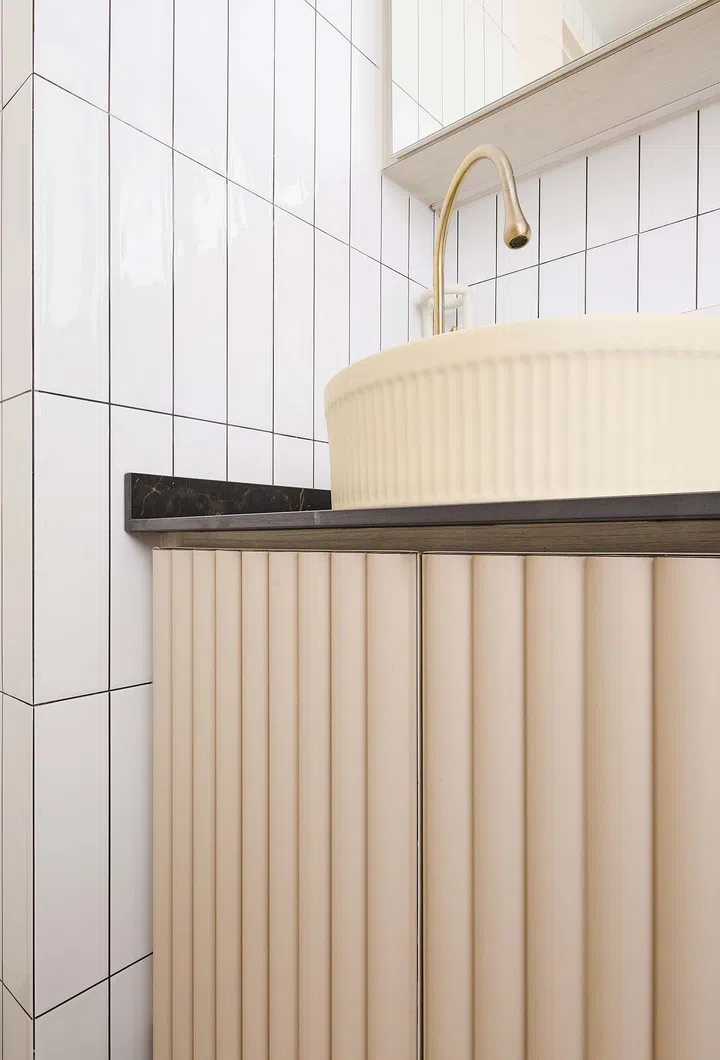 Bathroom vanity with a ribbed-profile sink and fluted paneling, blending tactile textures with elegant brass accents for a modern, cohesive look.