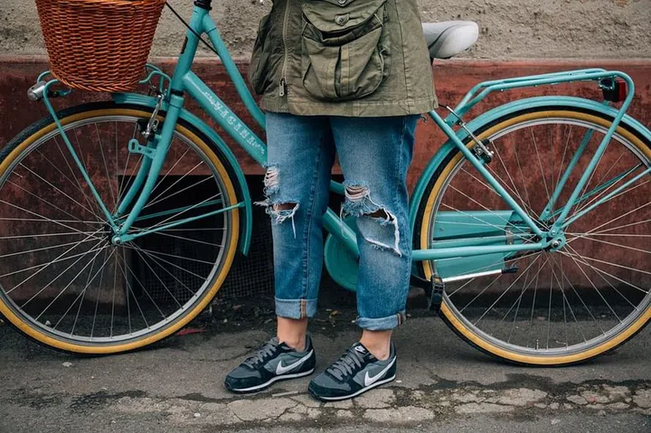 Half body shot of a woman in ripped, blue denim jeans, pictured against a bicycle.