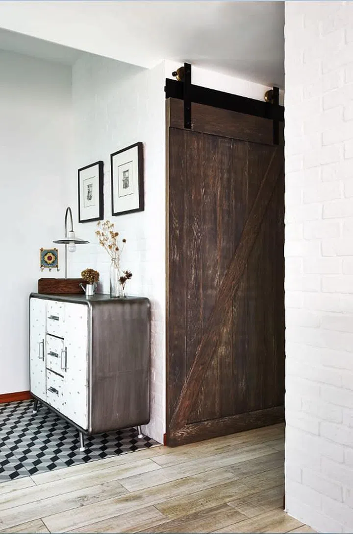 A barn-inspired door frames the entrance of the narrow L-shaped kitchen in this 3-bedroom condominium in Novena. Interior design by Museum Homes.