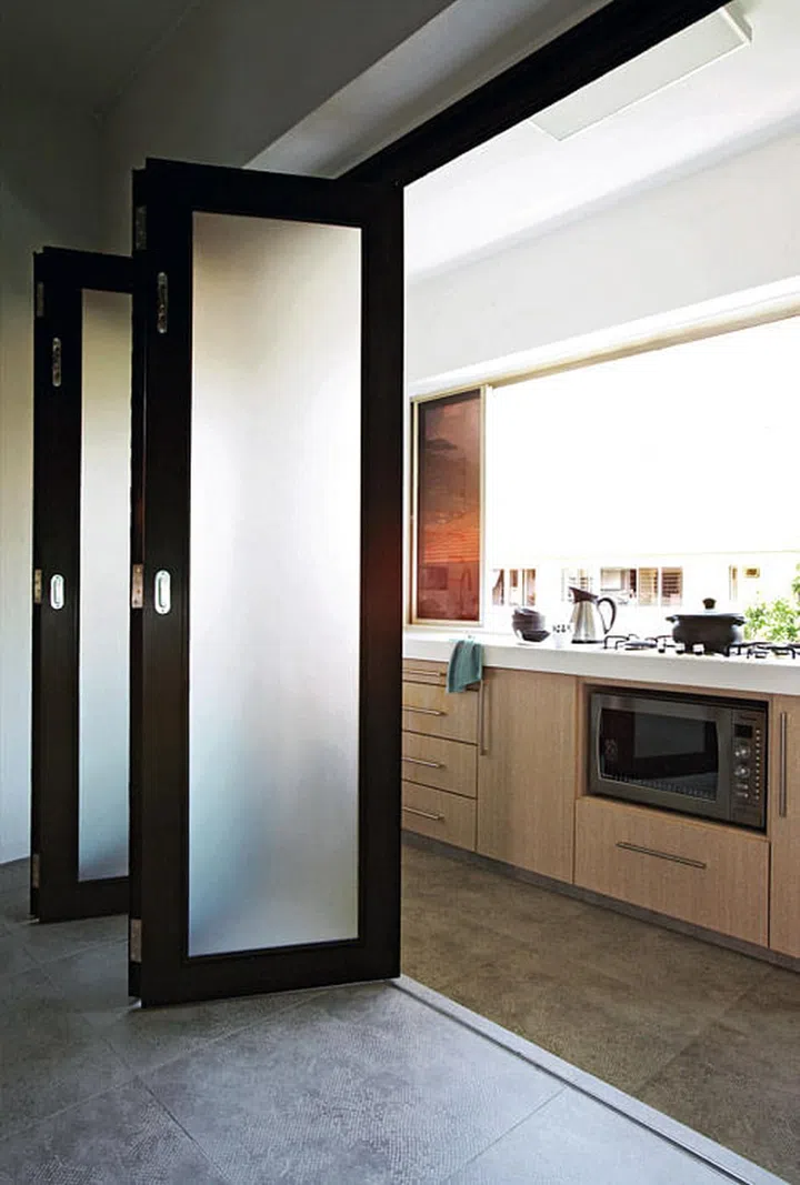 Frosted glass accordion-type folding doors conceal the kitchen, which was kept small as the homeowners opted to sacrifice some kitchen space for a fancier bathroom.
