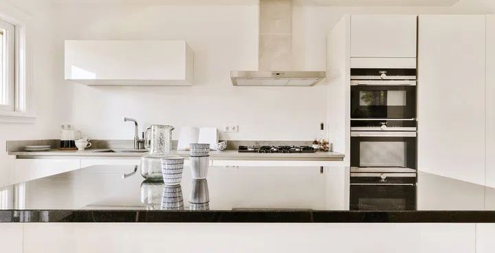 a white kitchen with black counter tops and stools in the center of the room, looking into the dining area