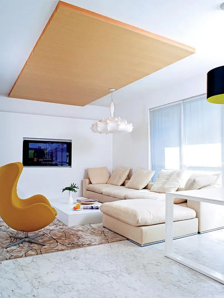The TV sits in a partition board that also conceals unsightly cable wires behind. A Zeppelin lamp by Marcel Wanders hangs from a oak veneer platform that was added to the ceiling for visual interest.