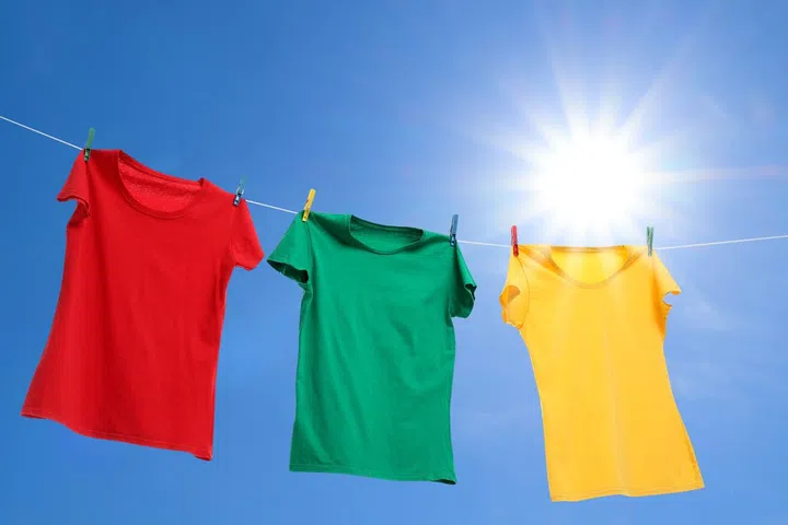 Colorful t-shirts drying on washing line against blue sky, low angle view.