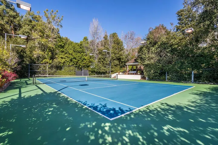 The tennis court is surrounded by numerous mature trees.