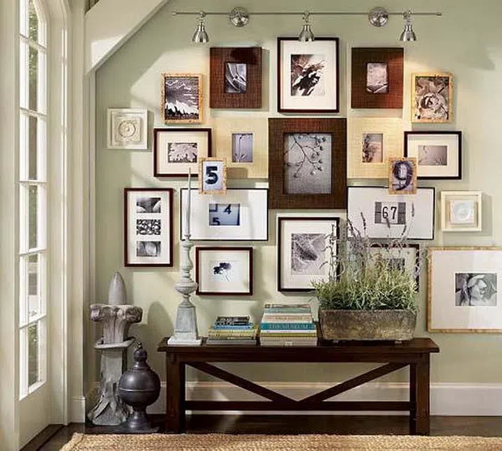 A series of traditional thick and thin wood photo frames arranged in an unrestricted and freestyle format on a wall, above a console bench.