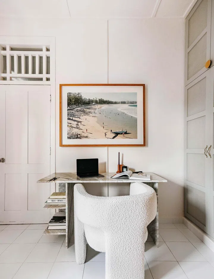 A marble study desk with a boucle chair, painting of beach hung on wall