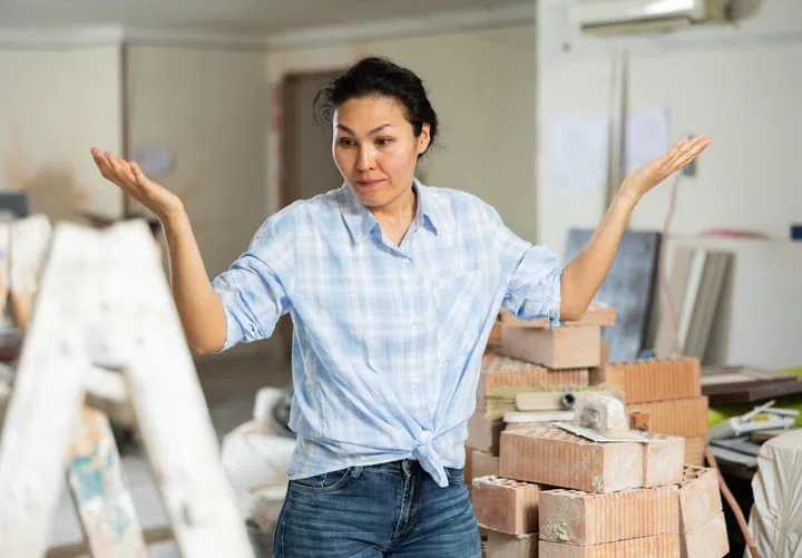 Portrait of frustrated young adult woman owner of apartment standing at indoor construction site, having problems with renovation.