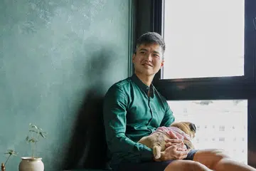 Bruce, aviation firefighter in his early 30s, and his pug poses for a photo by the window.