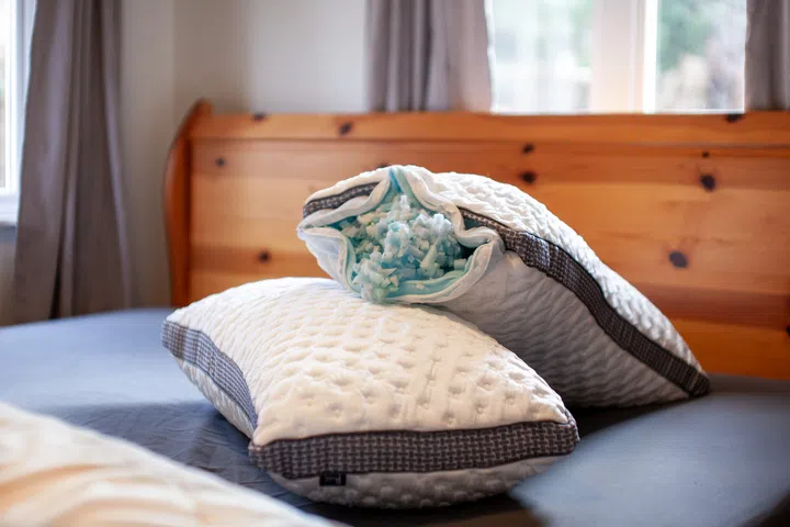 A set of two king size Gel Memory Foam pillows sit on a bed with the zipper open exposing the foam filling  of the insides. Pillow thickness is easily adjusted by removing the stuffing.