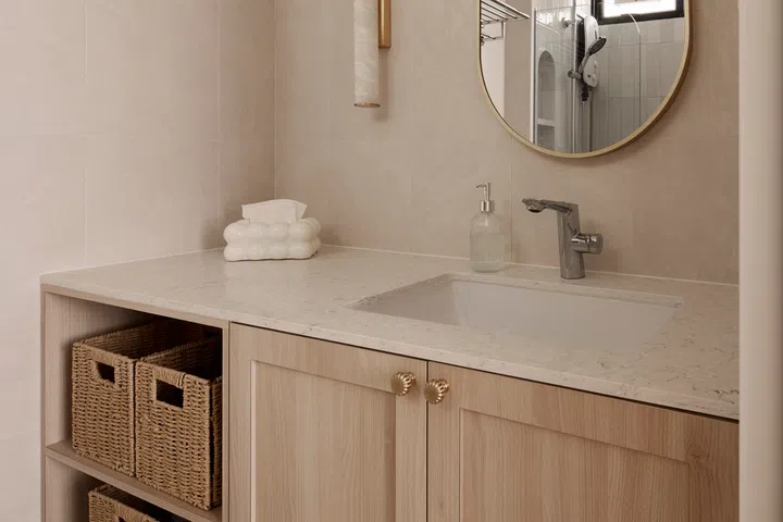 Light timber cabinetry, a stone-look countertop and gold accents continue the home’s warm, understated material palette.