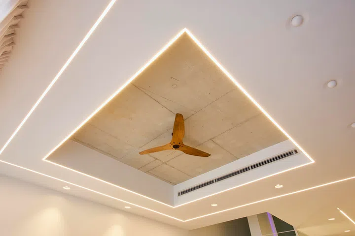 A recessed ceiling detail reveals the raw concrete slab above, framed by linear lighting that defines the space while keeping the overall palette restrained.