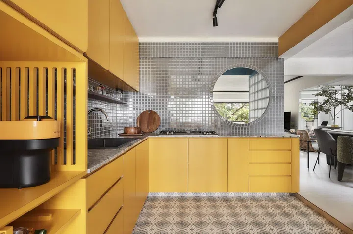 Bright yellow kitchen cabinets paired with grey mosaic walls, kitchen countertops, and Peranakan floor tiles in this 1,367 sq ft 5-room HDB at Bedok Reservoir Road. 