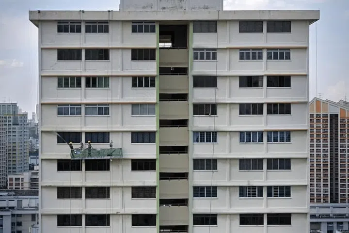 Frontal view of an old HDB building in Singapore with workers hanging outside a household working on the facade. Photo: ST