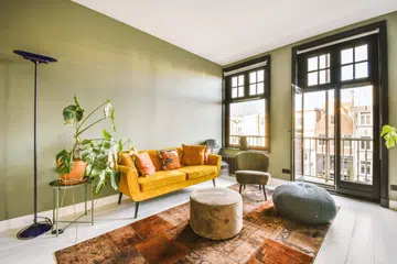 Interior of a bright living room with stylish furniture and decorations, as well as a glass door and black framed windows leading to a balcony on a sunny day