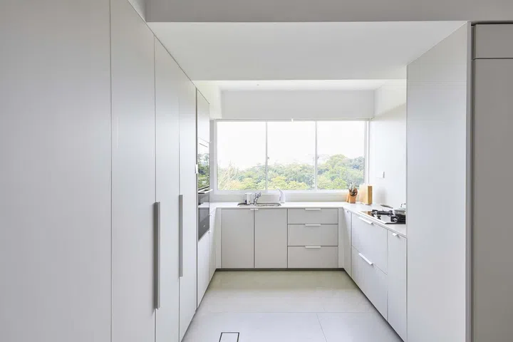 All white kitchen bears windows that overlooks the greenery in the vicinity.