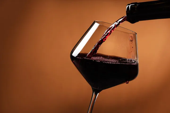 Pouring red wine into glass and bottles against brick wall background.