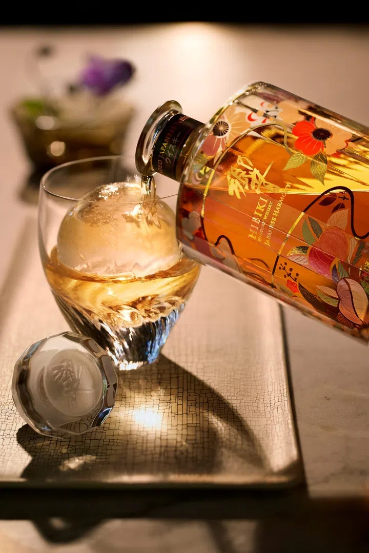 Hibiki Japanese Harmony whisky is poured over a large ice rock, highlighting its warm amber colour and elegant presentation.
