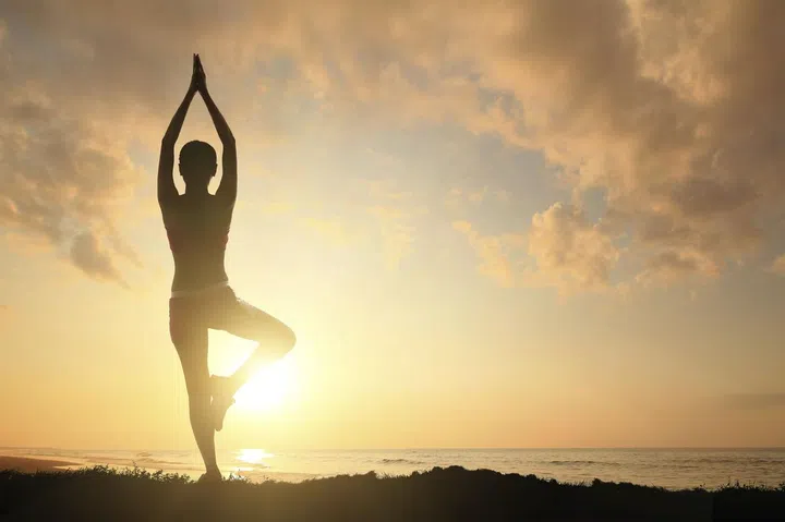 Young woman silhouette practicing yoga on the sea beach at sunset