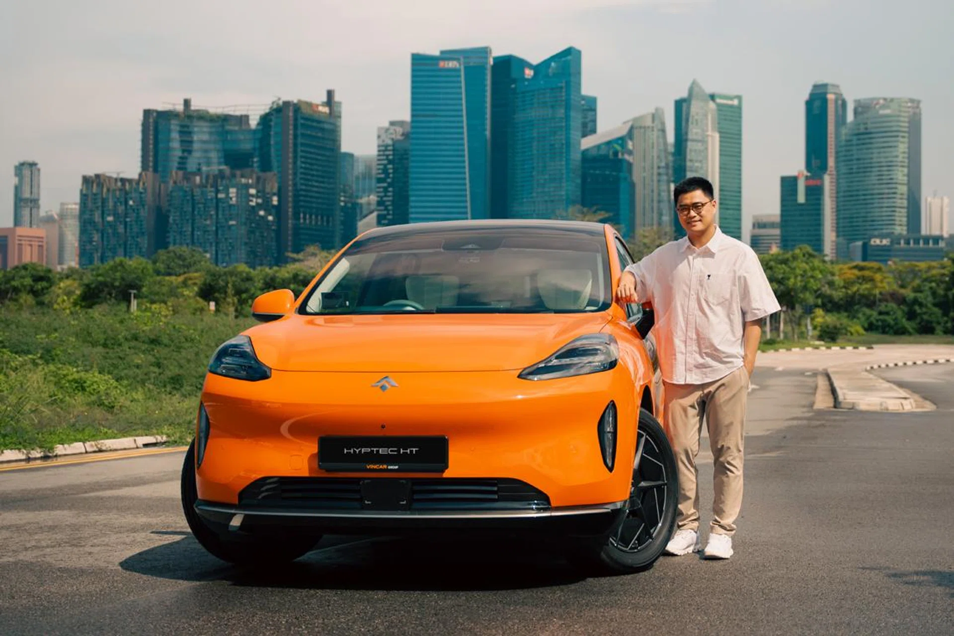 Ernest Tan, Vice-President of VINCAR Group, standing beside the orange GAC HYPTEC HT electric SUV against the Singapore skyline.