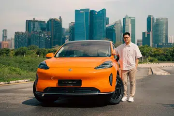 Ernest Tan, Vice-President of VINCAR Group, standing beside the orange GAC HYPTEC HT electric SUV against the Singapore skyline.